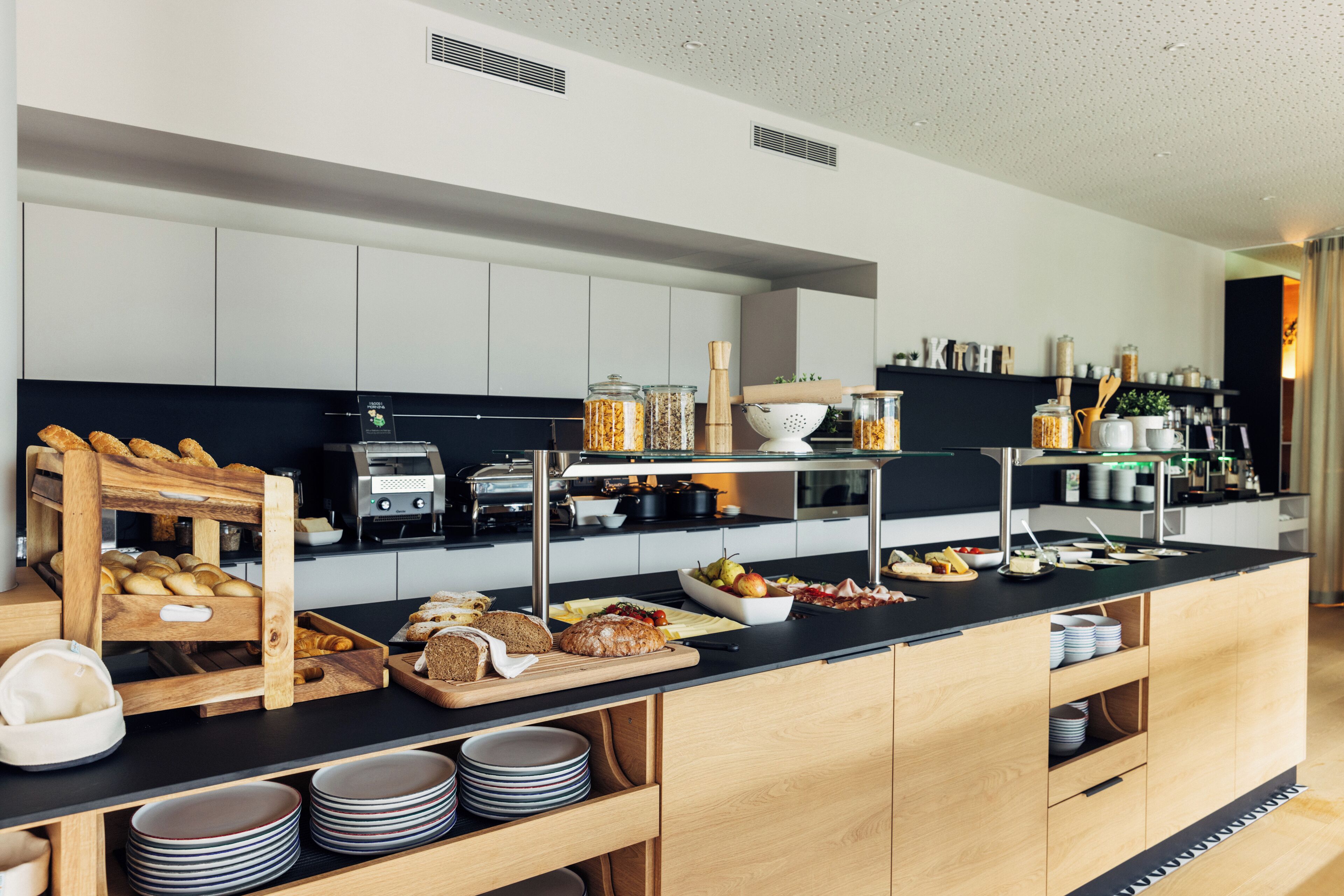 Cozinha moderna com bancada preta, armários de madeira e diversos alimentos e eletrodomésticos.