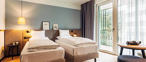 Habitación de hotel con dos camas, una mesita, una silla, una lámpara y vista al exterior.