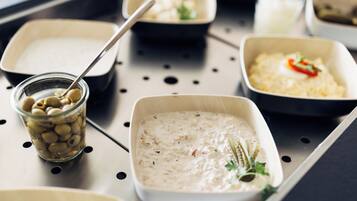 A tray with various food items including a creamy dish, a bowl of olives, and a container with a spoon.