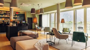 A modern hotel lobby with a bar area, seating arrangements, and large windows offering a view of the mountains. - harry's home Lienz hotel & apartments (Lienz)
