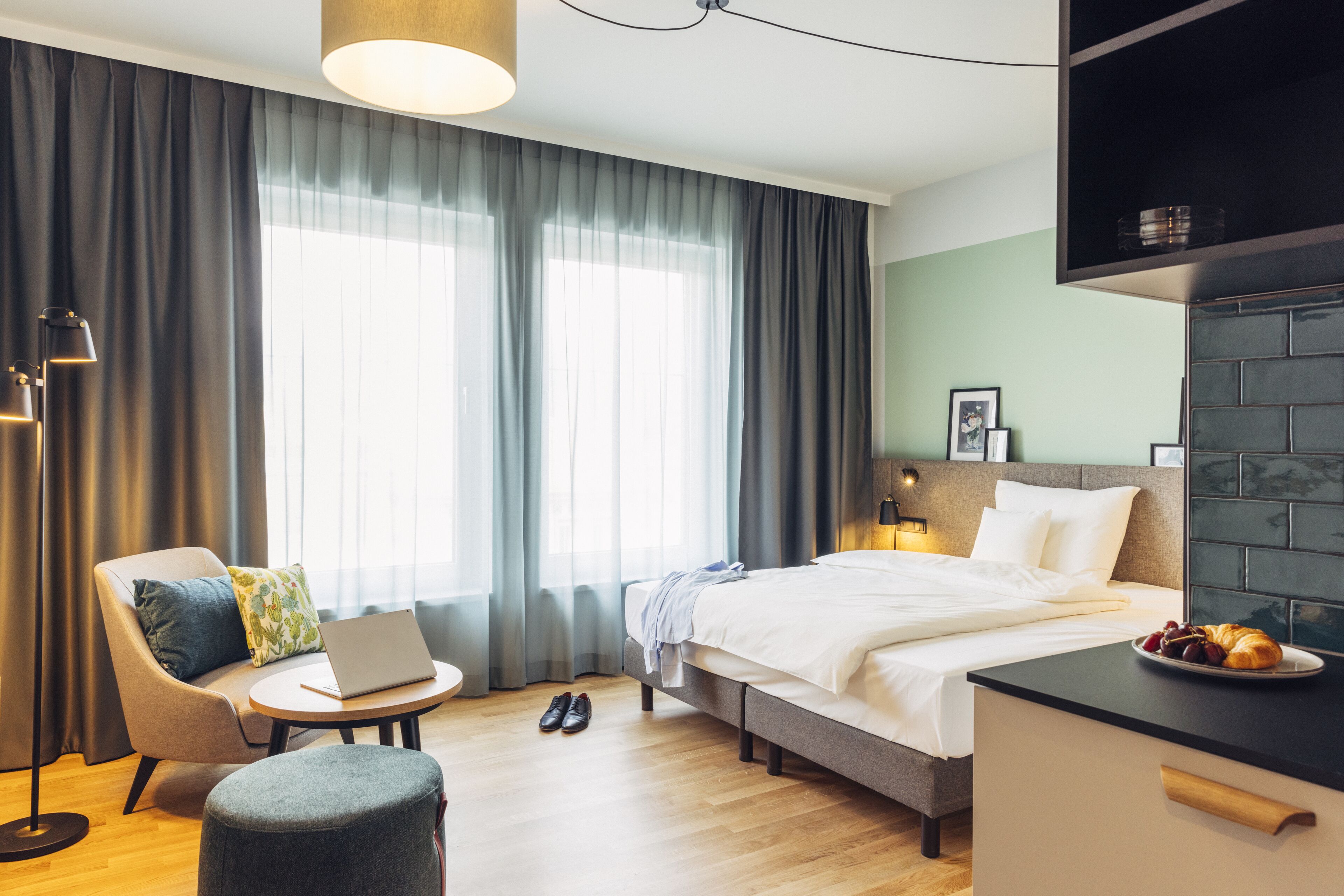 A modern hotel room with a bed, a desk, a chair, and a round table.