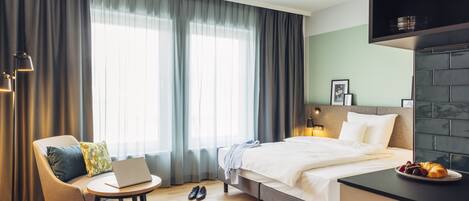 A modern hotel room with a bed, a desk, a chair, and a round table.