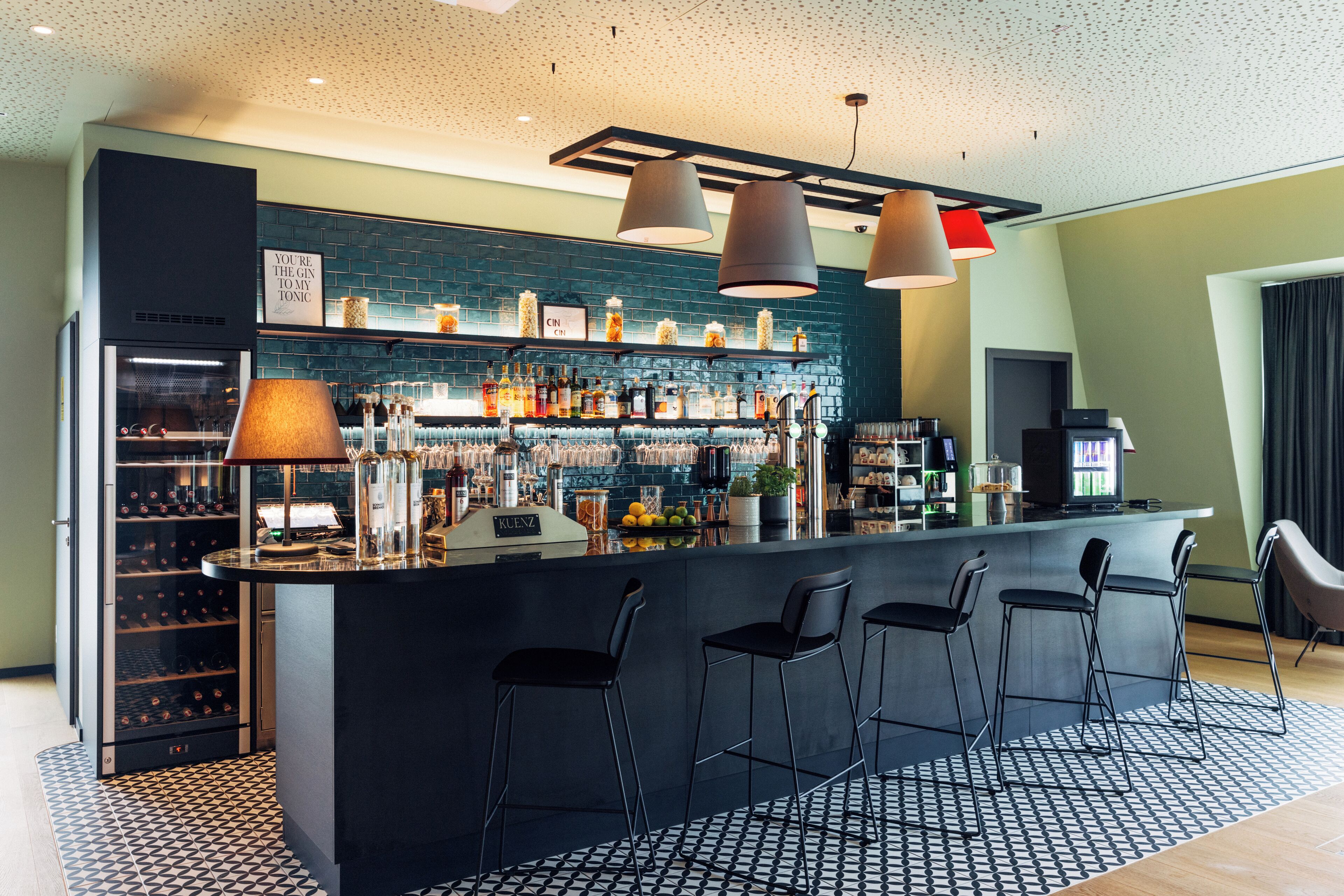 A modern bar area with a black countertop, bar stools, and a variety of bottles and glasses.