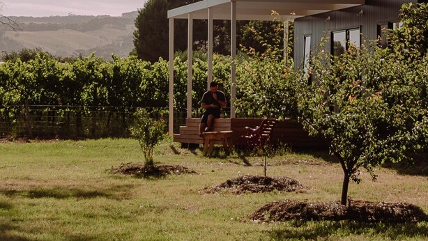 Une maison moderne dotée d’un patio couvert, d’un petit jardin et d’une personne assise sur un banc.