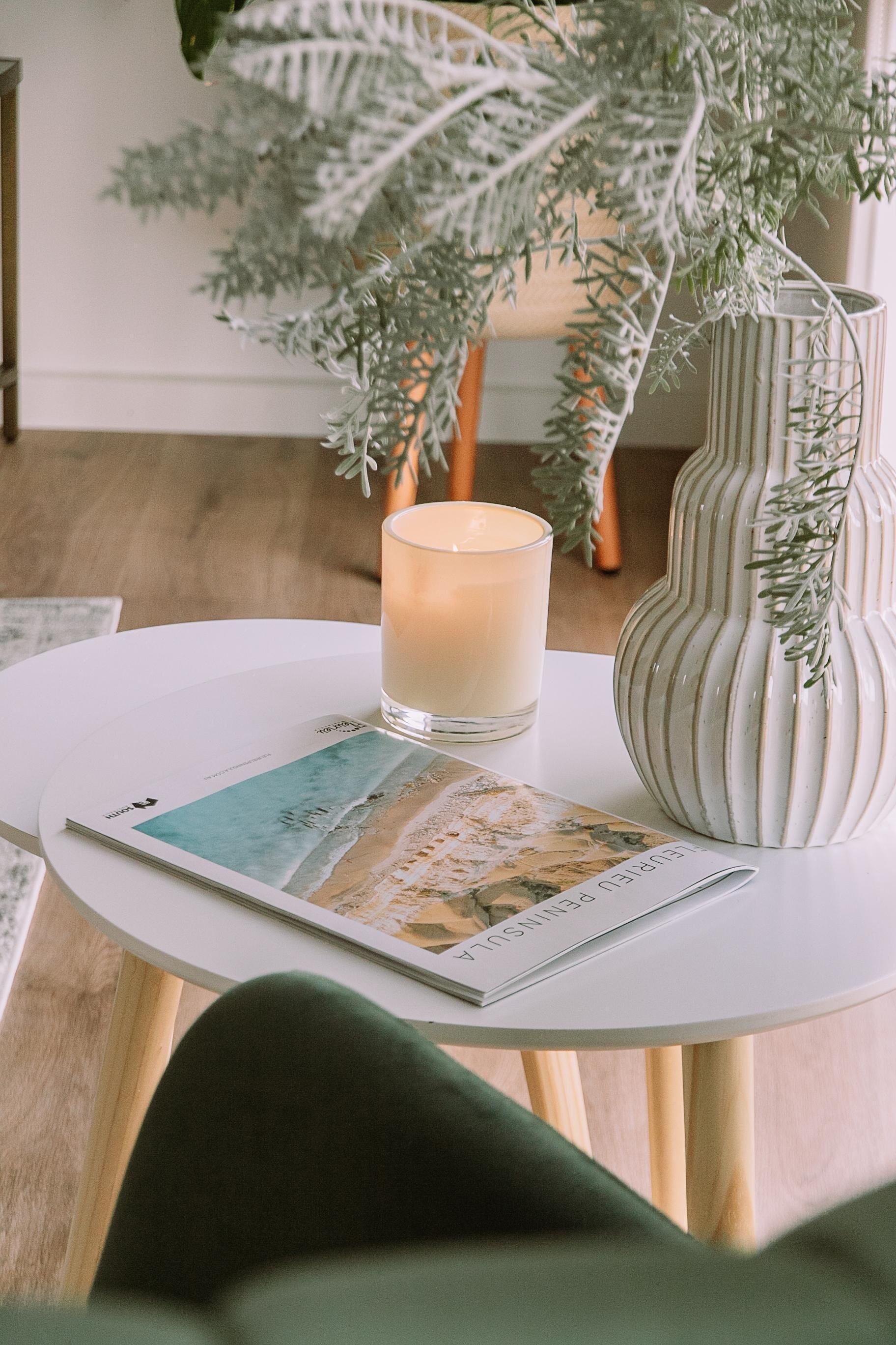 A white table with a candle, a decorative vase, and a magazine.