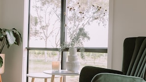 Un salon moderne avec une grande fenêtre, un fauteuil vert, une petite table et une plante en pot.