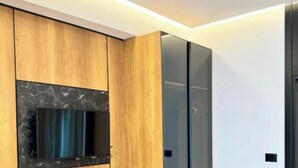 A modern room with a wooden desk, a flat-screen TV mounted on the wall, and a sliding glass door closet. - Hotel Joni Premium  (Ksamil)