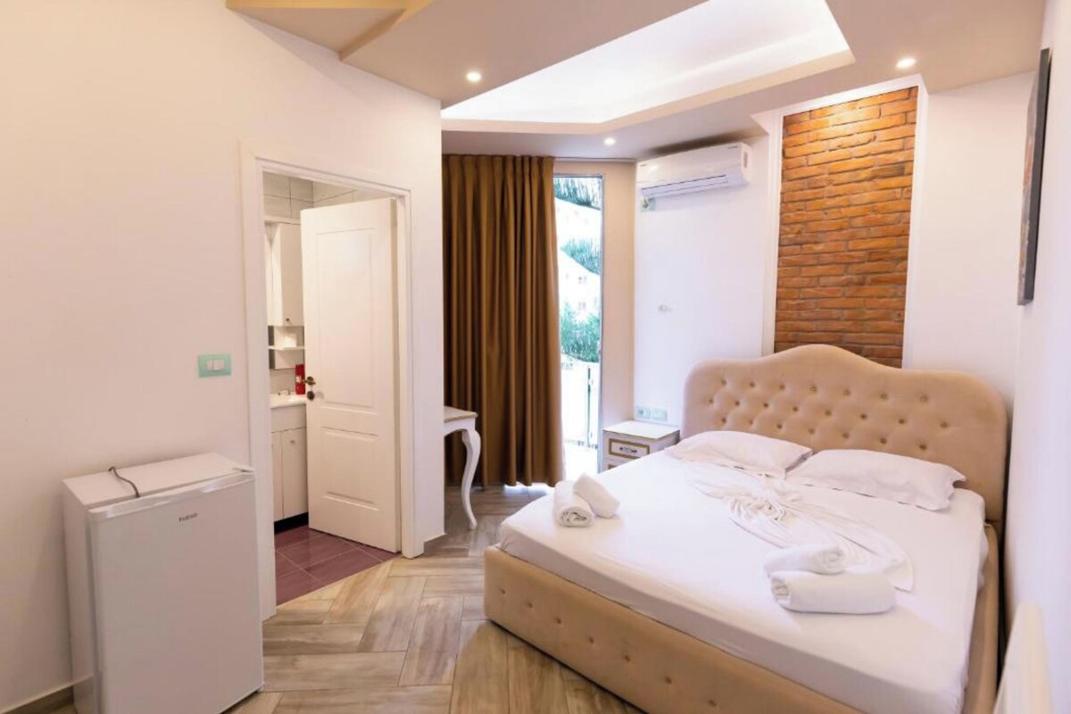 A hotel room with a bed, a desk, a refrigerator, and a window with curtains.