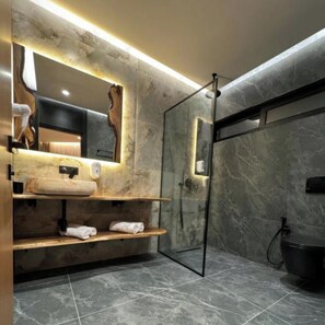 Une salle de bain moderne avec un sol en marbre, une douche en verre et une étagère en bois où sont posées des serviettes.