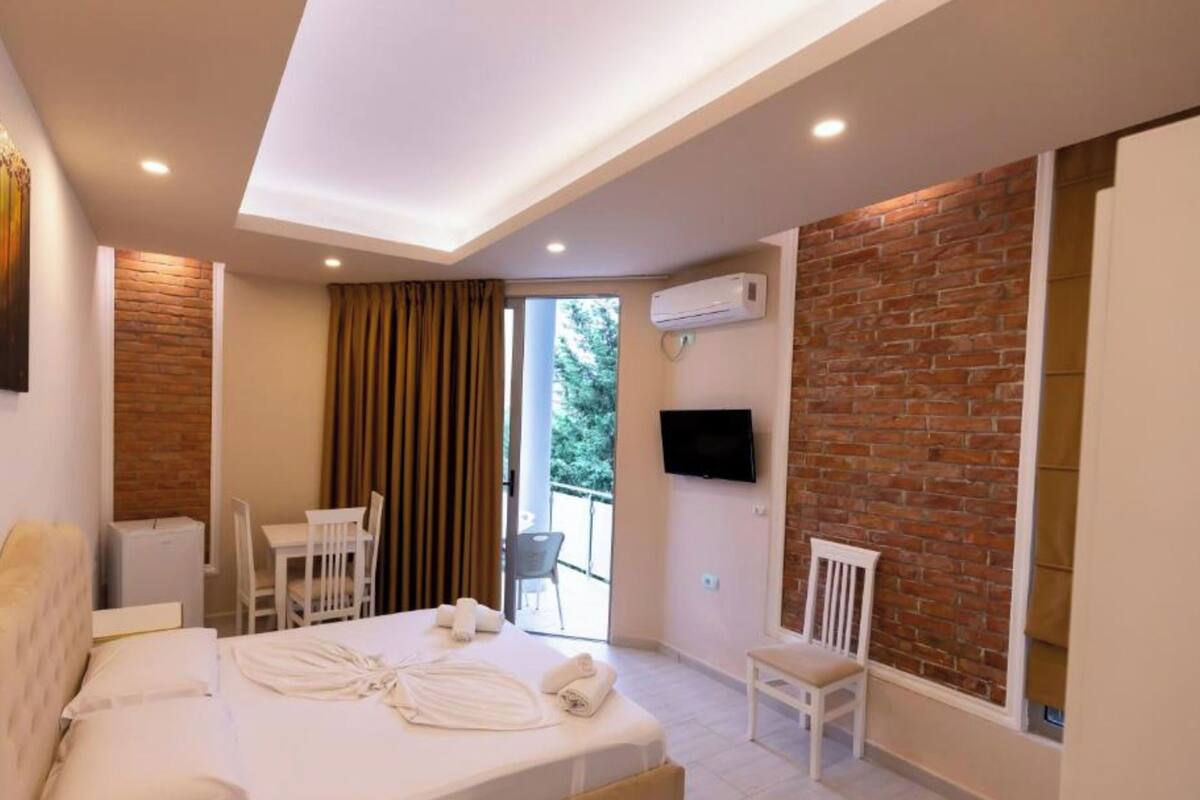 A modern hotel room with a bed, a desk, a chair, a TV, and a balcony with a view.