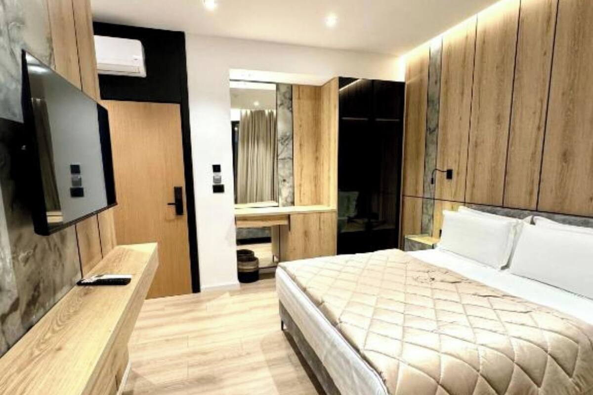 A modern bedroom with a large bed, wooden paneling, a flat-screen TV, and a built-in bench.
