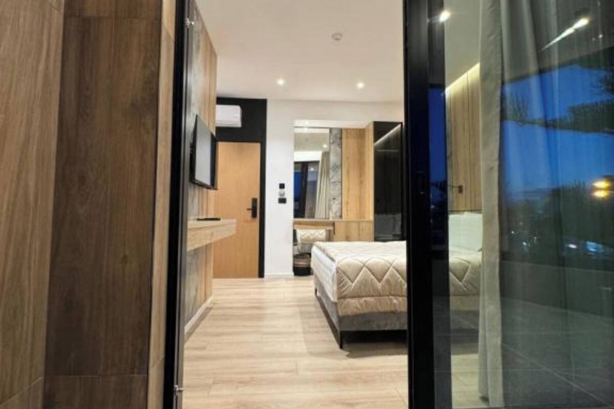 A modern bedroom with a large bed, wooden flooring, and a glass door leading to a balcony.
