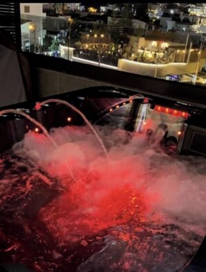 Un bain à remous dont la vapeur s’élève de l’eau, entouré d’une vue panoramique sur la ville illuminée la nuit.