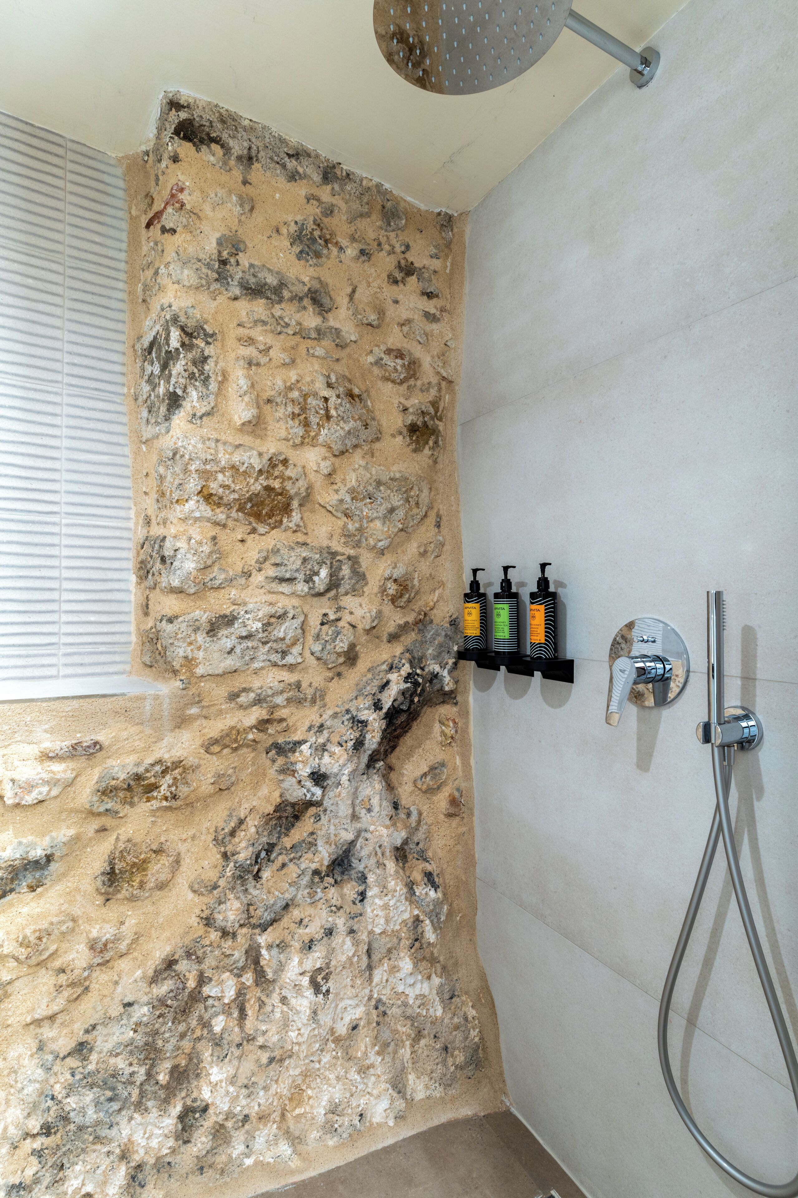 A bathroom with a stone wall, a shower, and a shelf with toiletries.