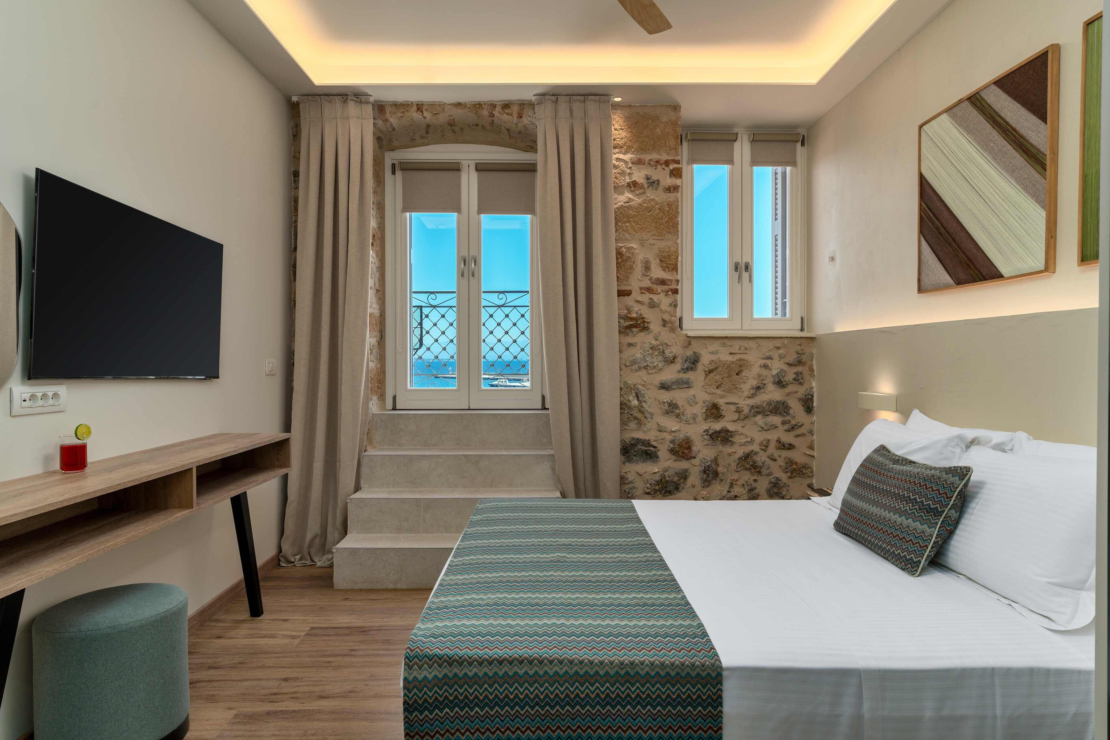 Habitación de hotel con cama, escritorio, televisor y una escalera que lleva a un balcón.