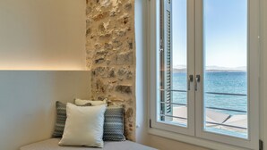 A bedroom with a stone wall, a bed with pillows, and a view of the sea through a window. - YeeOn Boutique Hotel, Gythio - Historic Hotels of Europe (East Mani)