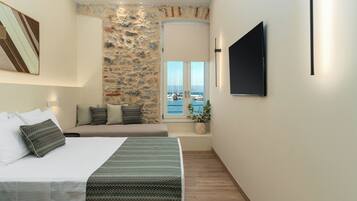 Una habitación de hotel moderna con una cama grande, una zona de estar con vistas al mar y un televisor de pantalla plana montado en la pared.