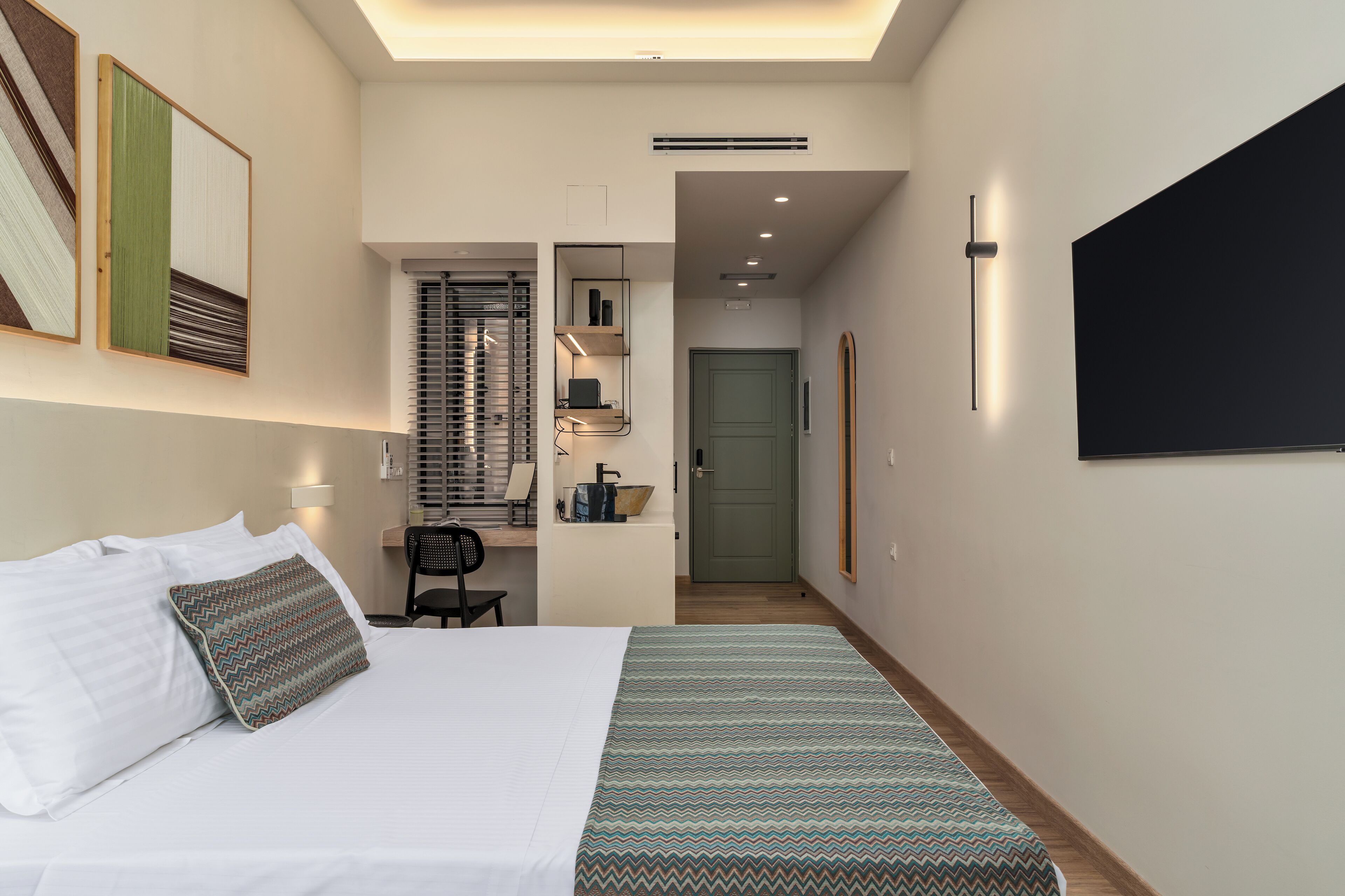 A hotel room with a bed, a desk, a chair, a TV, and a door.