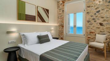 A bedroom with a bed, a chair, a wall-mounted artwork, and a stone wall.