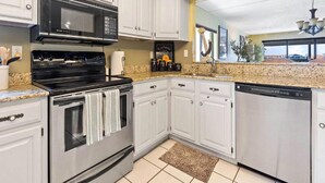 A modern kitchen with white cabinetry, stainless steel appliances, granite countertops, and a view of the cityscape through a large window.
