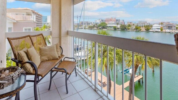 A balcony with wicker furniture, a view of a marina, and buildings in the background.