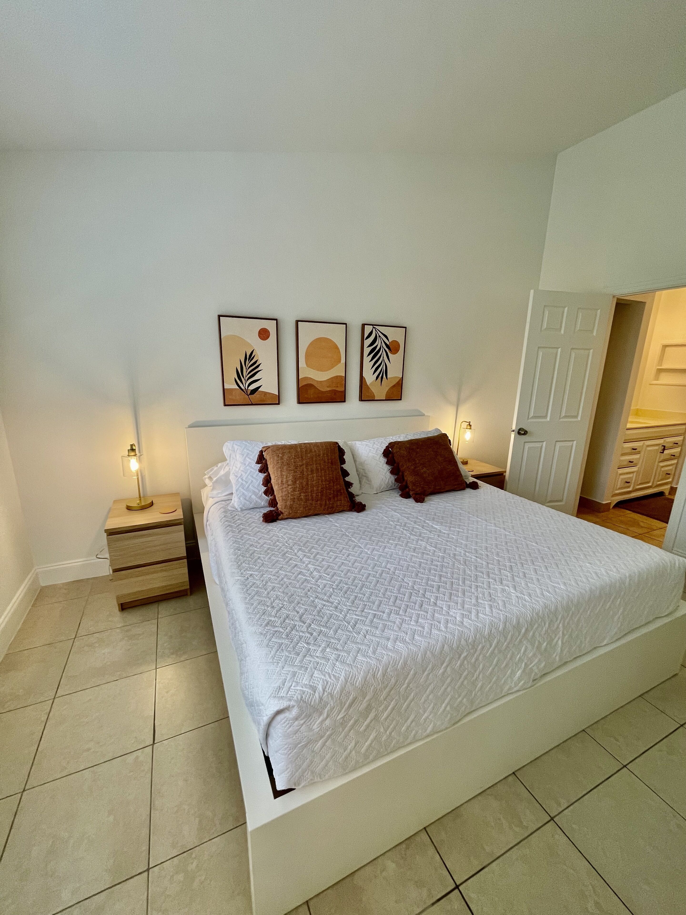 A bedroom with a large bed, two bedside tables, and three wall-mounted artworks depicting abstract sun and leaf designs.