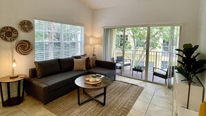 Ett vardagsrum med en soffa, ett soffbord och en lampa. Det finns en balkong med stolar och en växt.