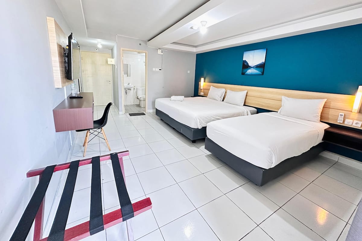 A hotel room with two beds, a desk with a chair, a TV, and a bathroom visible through an open door.