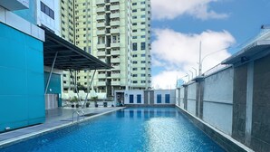 A swimming pool with a clear blue water surface, surrounded by high-rise buildings and a clear sky. - IZI COZI HOTEL KEMAYORAN  (Jakarta)