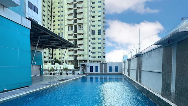 A swimming pool with a clear blue water surface, surrounded by high-rise buildings and a clear sky. - IZI COZI HOTEL KEMAYORAN  (Jakarta)