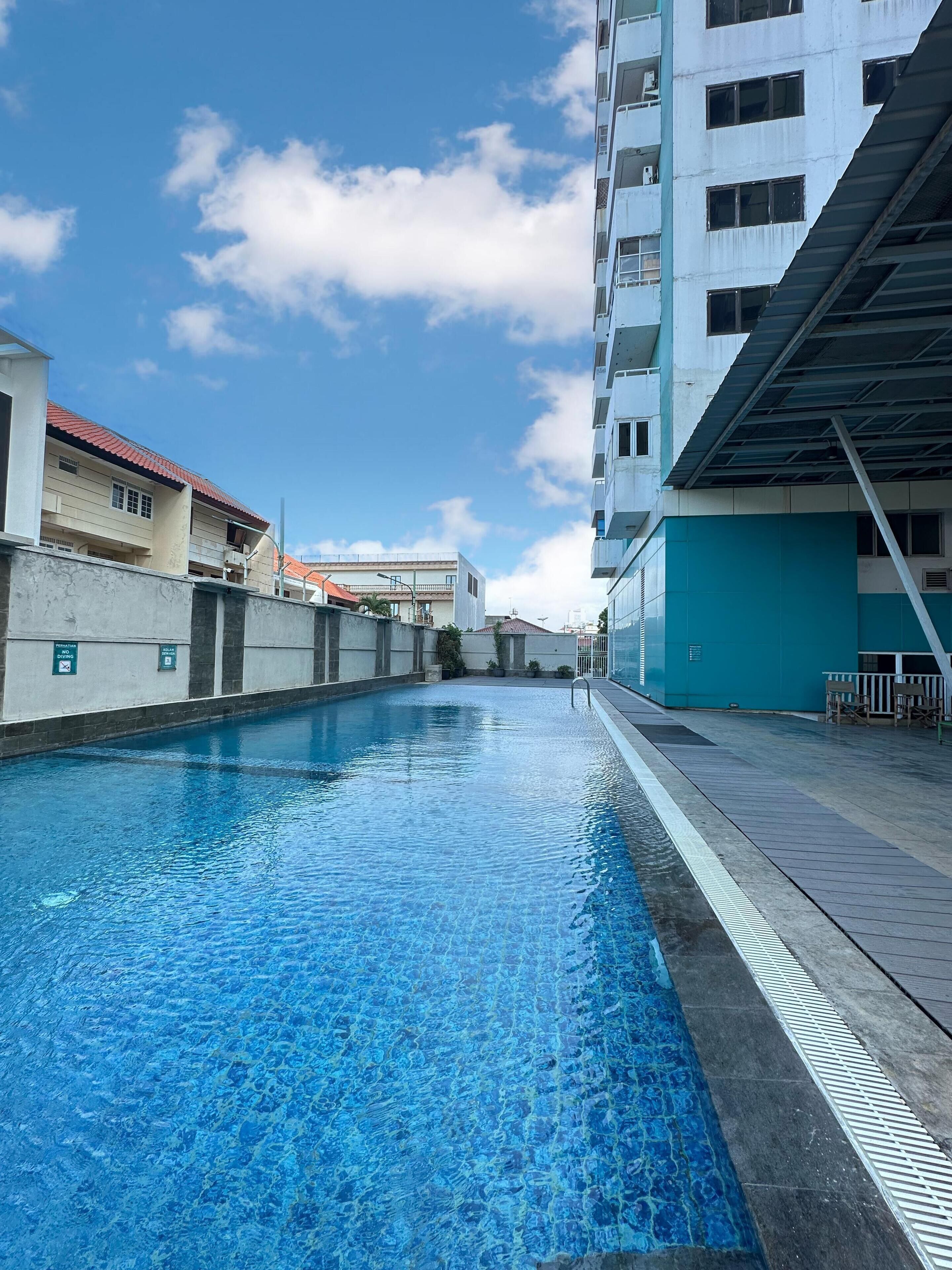 Une piscine à l’eau d’un bleu limpide, entourée d’un mur en béton et bordée d’un bâtiment au toit rouge.
