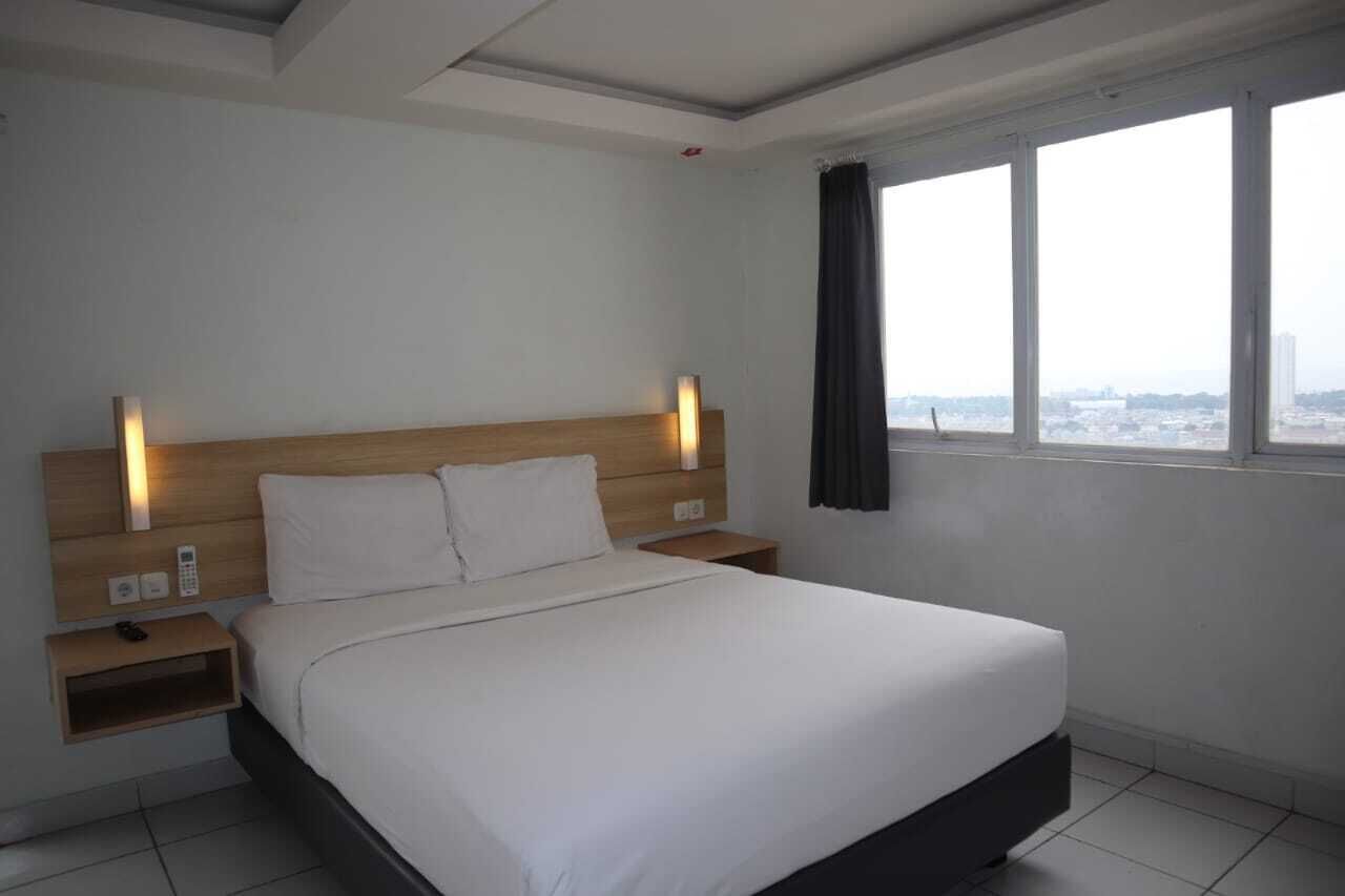 A hotel room with a large bed, bedside tables, a headboard with integrated lighting, a window with curtains, and a city view.