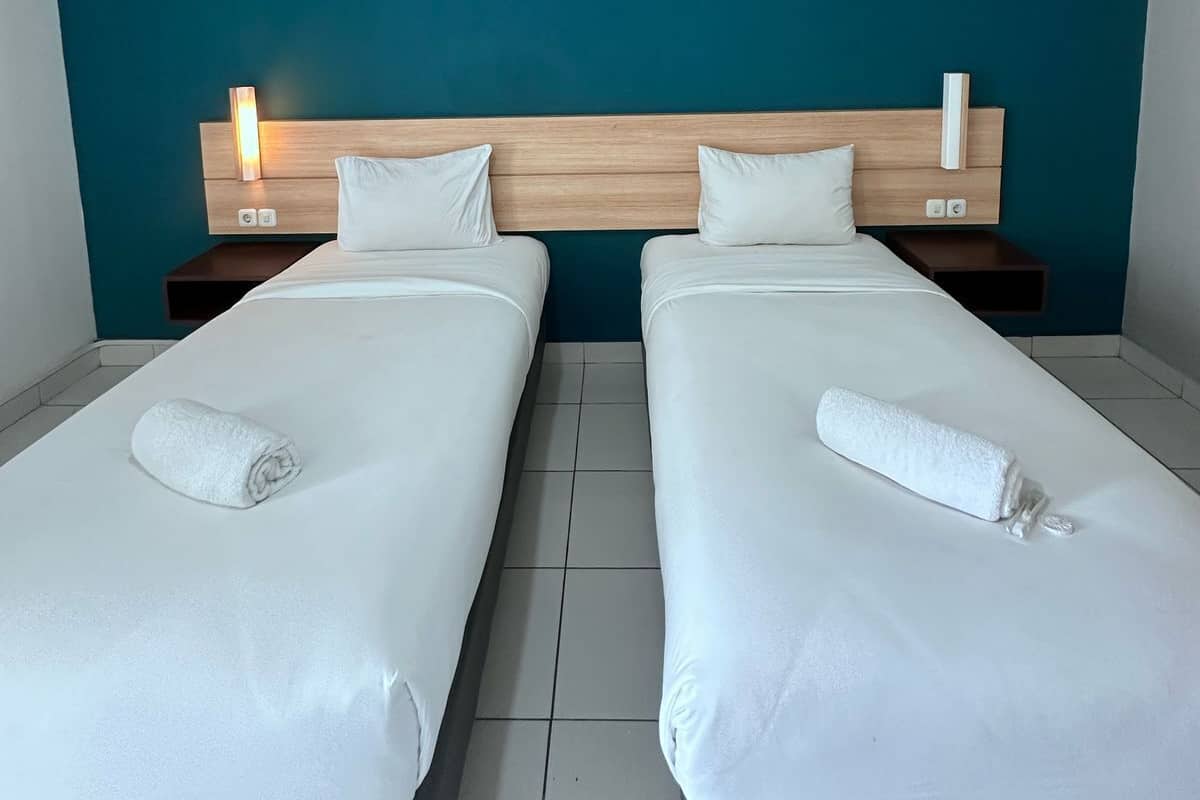 A hotel room with two single beds, a wooden headboard, bedside tables, and a teal accent wall.