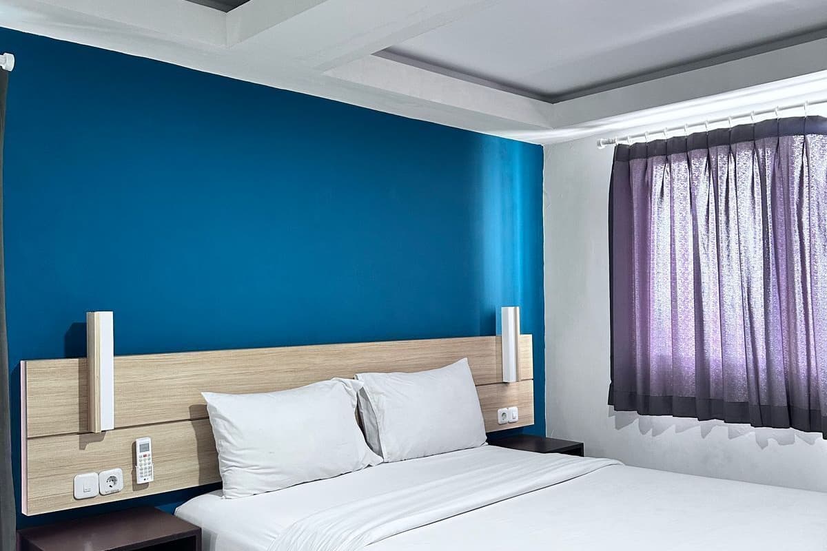 A modern hotel room with a large bed, a wooden headboard, a nightstand, and a window with purple curtains.