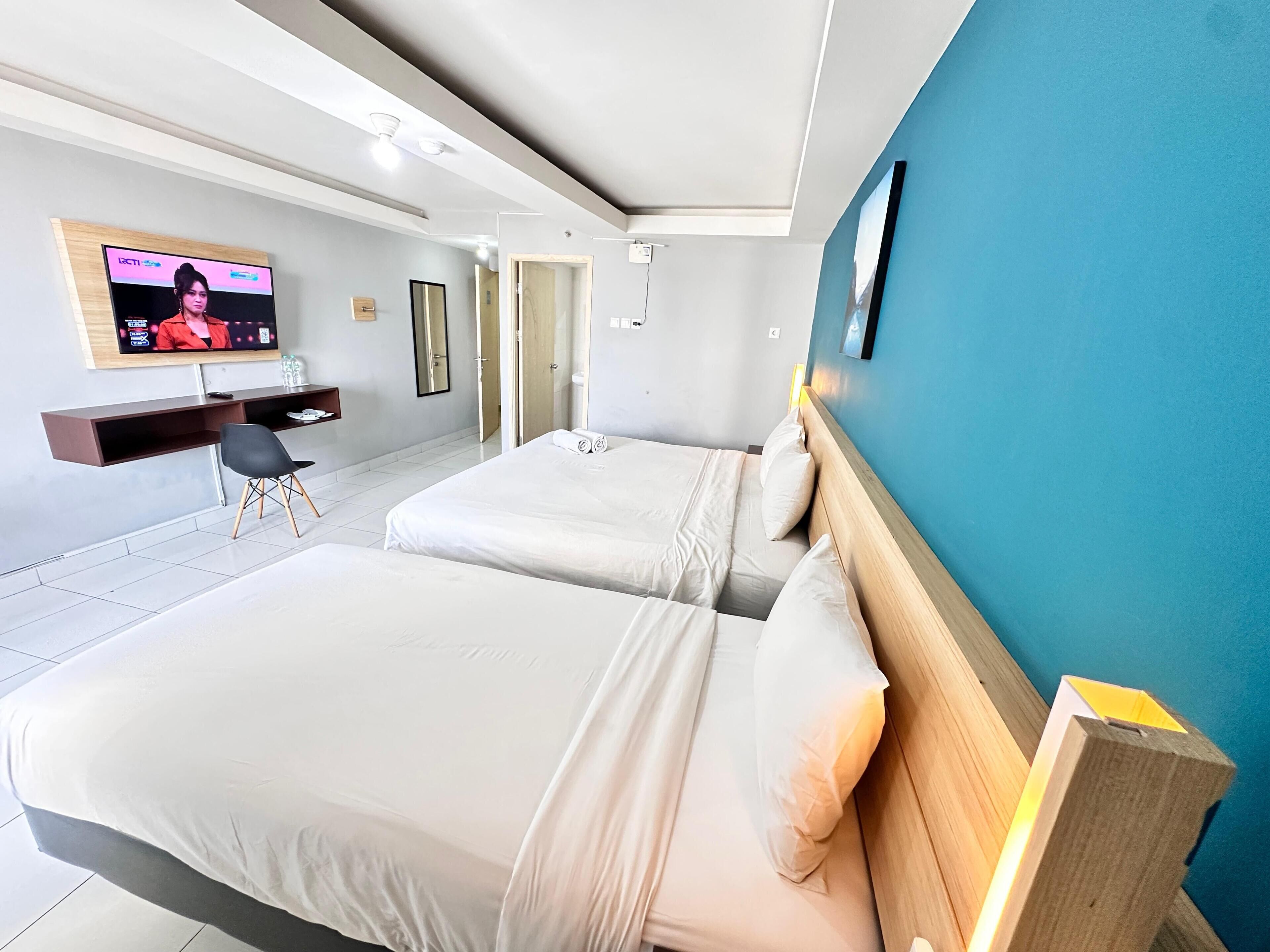 Habitación de hotel con dos camas, televisión, escritorio y una silla.