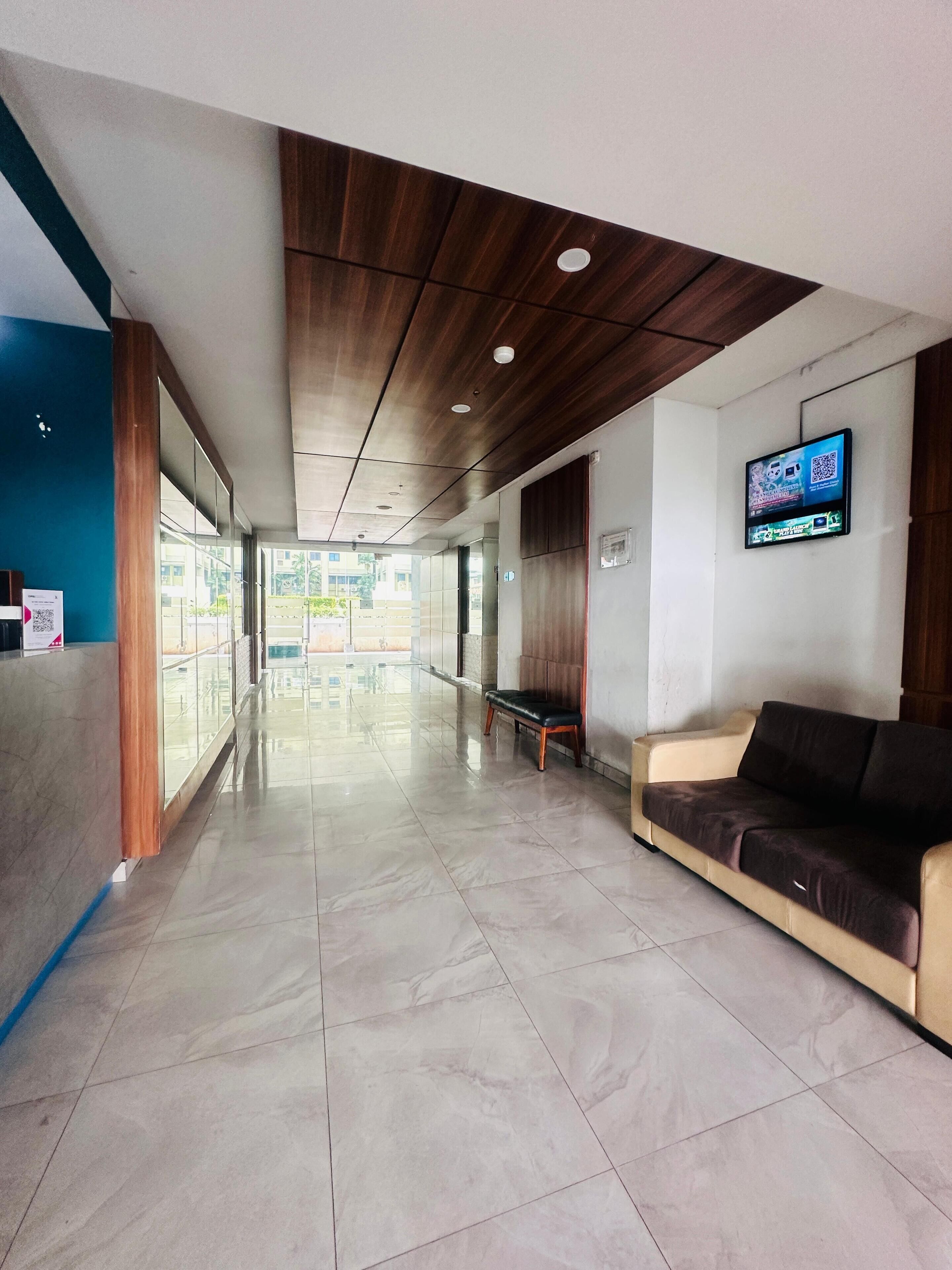 Un espace d’accueil moderne avec un plafond en bois, un comptoir d’accueil, un espace d’attente doté d’un canapé et un écran de télévision diffusant une publicité.
