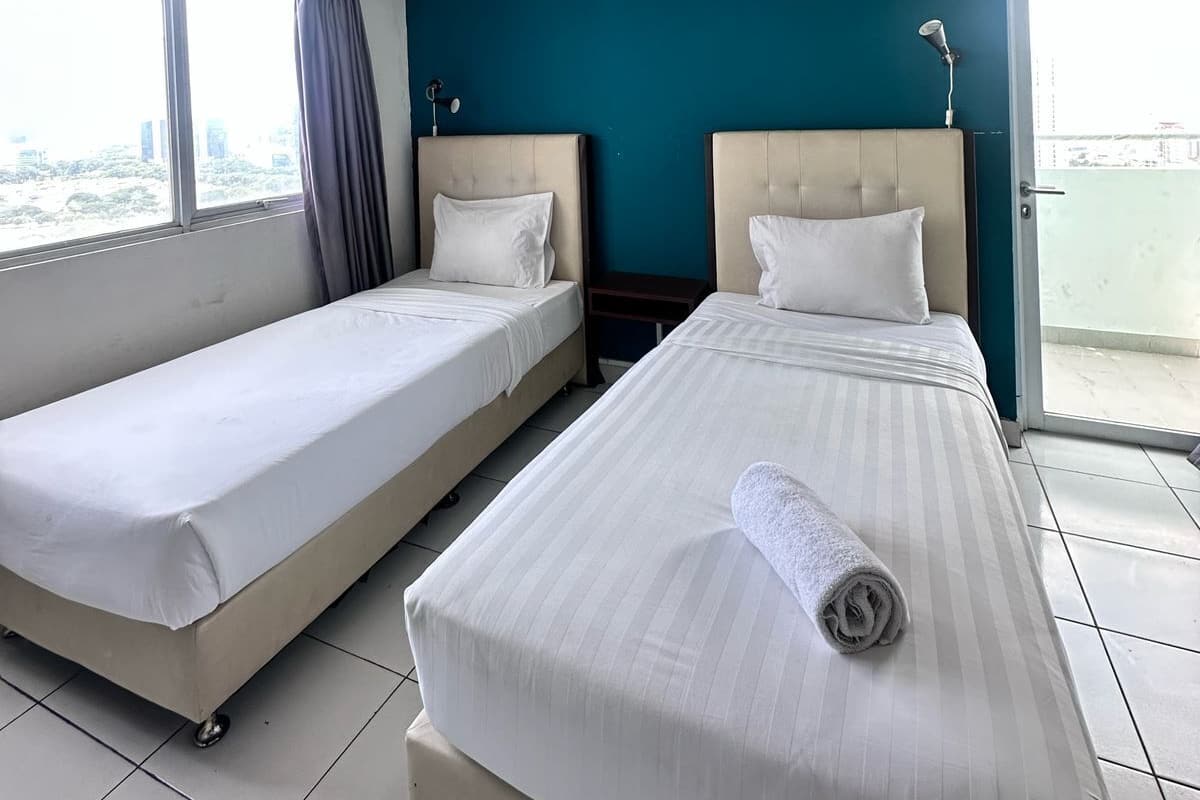 A hotel room with two beds, a ceiling fan, and a view of the city through the window.