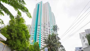 A tall, modern building with a prominent vertical feature, surrounded by greenery and urban infrastructure. - IZI COZI HOTEL KEMAYORAN  (Jakarta)
