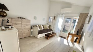 Et moderne, veloplyst rum med et spisebord, en sofa, et lille tekøkken med komfur og en skydedør, der fører til et udendørs område.