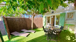 En terrasse med et bord og stole, et overdækket siddeområde og udsigt til huset.