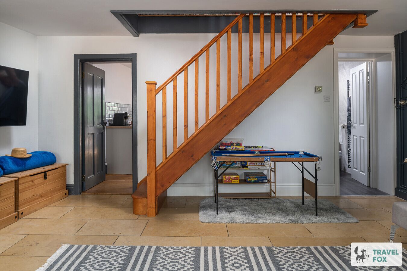 A staircase leading to a second floor, a small table with toys, a television on the wall, and a patterned rug on the floor.