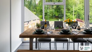 Un comedor con una mesa de madera preparada para cuatro, ventanas amplias y vistas a un jardín.