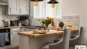 A modern kitchen with white cabinets, a wooden countertop, two pendant lights, and a breakfast setup with eggs, fruit, and pastries. - Katie`s Cottage and Hot Tub  Snowdon 20mins drive (Snowdonia & North Wales)