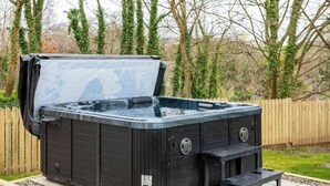 A black hot tub with a lid open, set on a wooden deck with a wooden fence in the background. - Katie`s Cottage and Hot Tub  Snowdon 20mins drive (Snowdonia & North Wales)