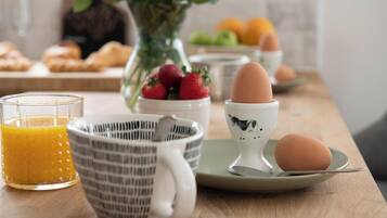 Colazione con un bicchiere di succo d'arancia, una tazza a righe, una ciotola di fragole, un portauovo in ceramica e un piatto con un uovo.