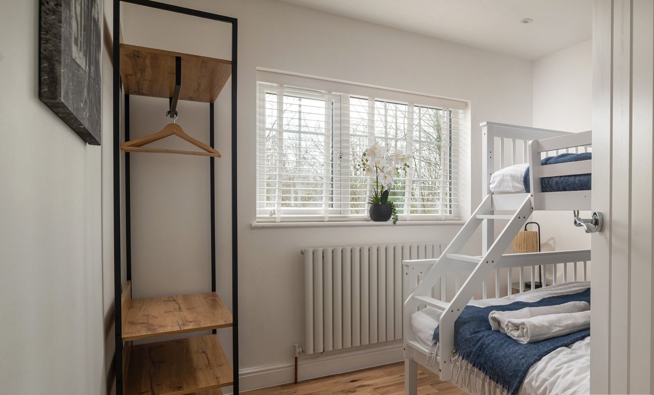 Ein Schlafzimmer mit Etagenbett, einer Holzregaleinheit, einem Heizkörper und einem Fenster mit Jalousien.
