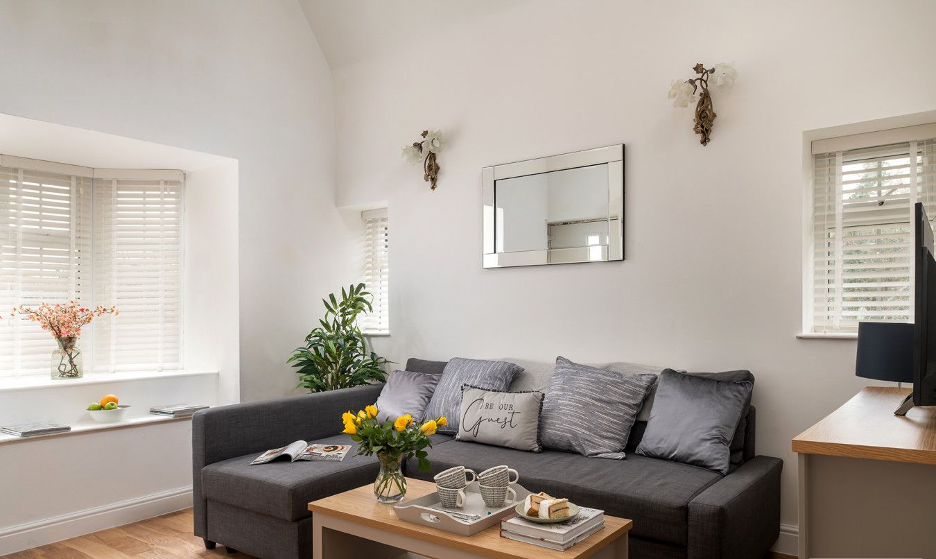 A modern living room with a grey sofa, a wooden coffee table, and a large mirror on the wall.