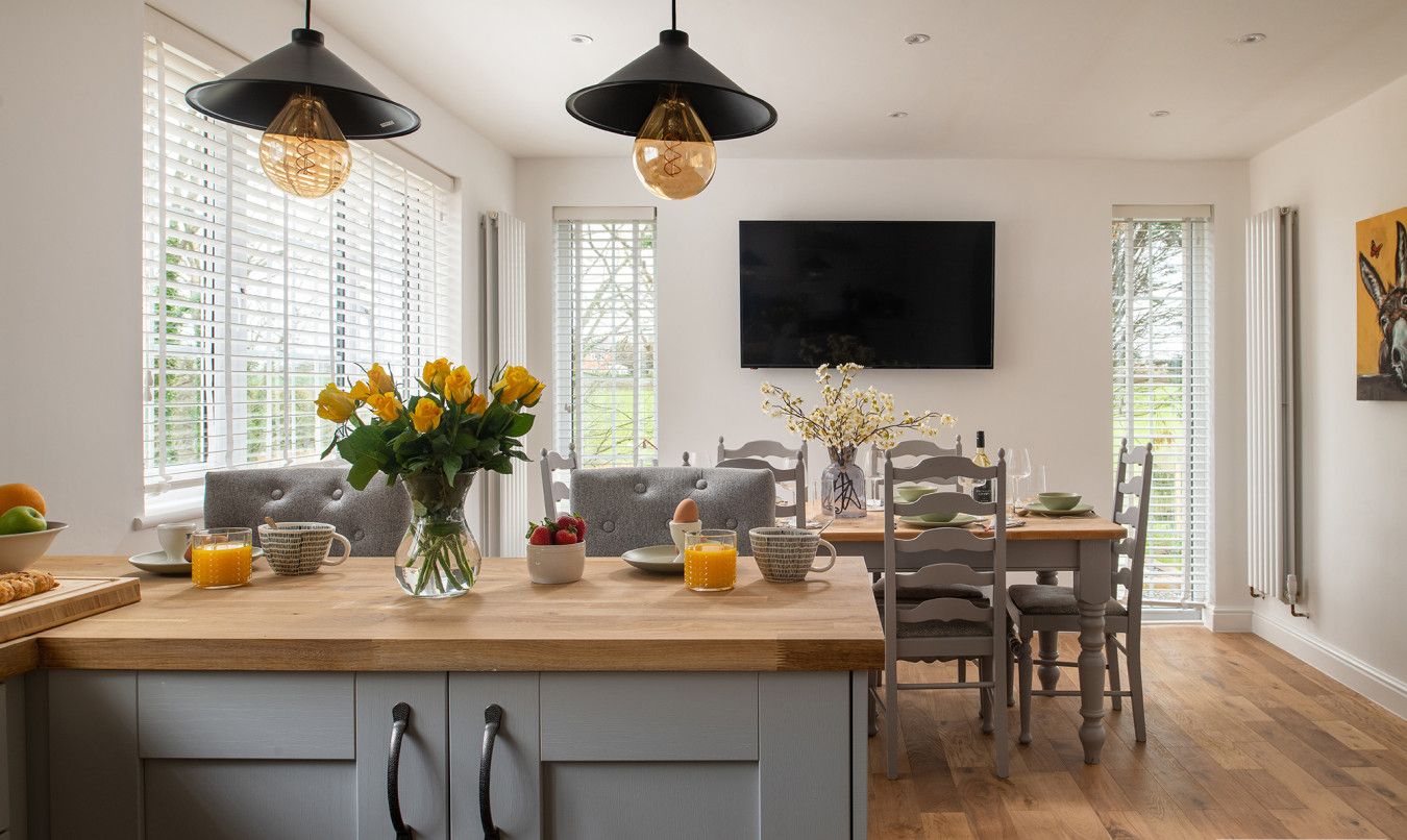 A modern kitchen with a central island, pendant lighting, and a dining area with a wooden table and chairs.