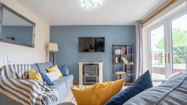 Una sala de estar con un sofá gris, una manta a rayas, un cojín amarillo, una estantería y una chimenea.