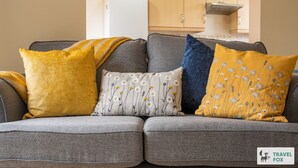 Un sofá gris con cuatro cojines en tonos amarillo, azul, blanco y mostaza.